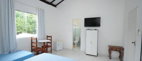 Un dormitorio con dos camas, televisor, armario, una mesita y una ventana con cortinas.