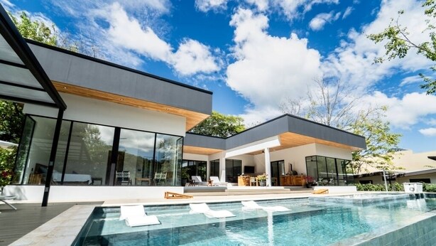 Ett modernt hus med en swimmingpool, stora fönster och en täckt uteplats.