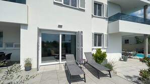 Moderni kaksikerroksinen rakennus, jossa on patioalue, jossa on kaksi aurinkotuolia ja pieni pöytä.