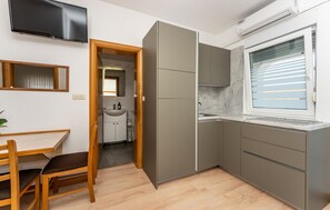 A compact kitchen with a built-in refrigerator, a window with blinds, and a television mounted on the wall. - Nice apartment in Vir with WiFi (Vir)