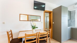 Ein Essbereich mit Tisch und Stühlen, einem an der Wand befestigten Fernseher und einem Spiegel über dem Tisch.