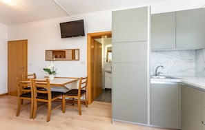 Ett kompakt kök med en diskho, en tv som är monterad ovanför bänkskivan och en matplats med ett bord och stolar.