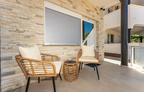 Ein Balkon mit Korbmöbeln, einer Steinmauer und einem Fenster mit Rollläden.