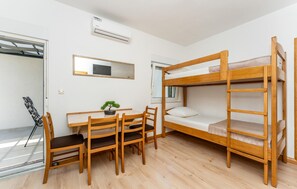 Een kamer met een stapelbed, een bureau met stoelen, een potplant en een spiegel aan de muur.