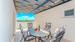 Un patio techado al aire libre con una mesa y sillas, una botella de vino y vistas al cielo y edificios al fondo.