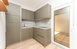 Eine kompakte Küche mit integriertem Spülbecken, einer Marmor-Spritzschutzwand und einer Glastür zum Außenbereich.