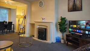 Ein Wohnzimmer mit Kamin, einer Uhr, einem Fernseher und einem Essbereich.
