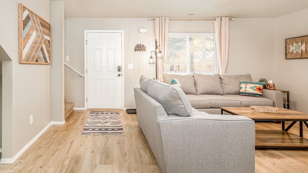 Ein Wohnzimmer mit grauem Sofa, Couchtisch aus Holz und einem gemusterten Teppich.