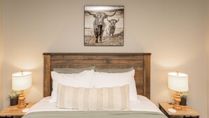 Ein Schlafzimmer mit einem hölzernen Kopfende, zwei Nachttischen mit Lampen und einem gerahmten Bild von Kühen an der Wand.