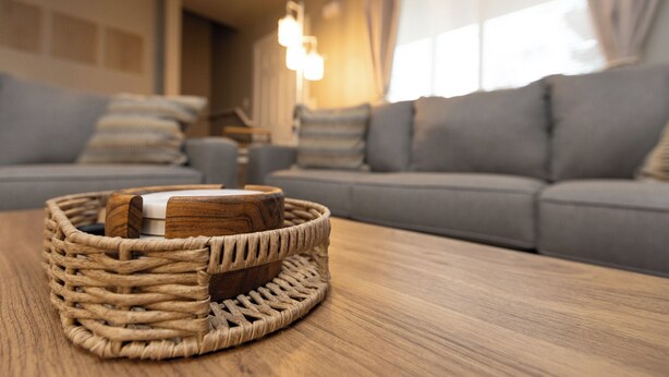 Een rieten mand met een houten doos op een houten tafel in een woonkamer met een grijze bank en een hanglamp.