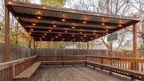Een houten terras met banken en een overdekt gedeelte met lichtjes.