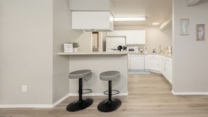 Una cocina moderna con armarios blancos, una isla central con taburetes y un microondas.