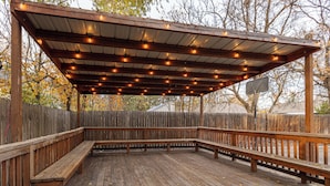 Una terraza de madera con bancos y un espacio cubierto con luces colgantes.