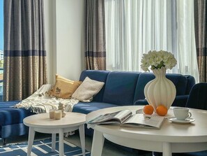 Una sala de estar con un sofá azul, una mesa de centro blanca y un jarrón con flores.