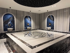 Un baño lujoso con un amplio suelo de mármol, tres nichos de arco con detalles decorativos y un diseño de techo que simula un cielo estrellado.