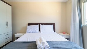 A hotel room with a bed, two pillows, a nightstand, a lamp, a towel, and a wardrobe. - Apt w/ 2 Bedrooms and Barbecue Grill Fdc0005 (Florianópolis)