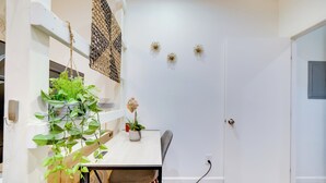 Un coin repas avec une table blanche, des chaises et des plantes suspendues. On y trouve une porte avec une poignée et un luminaire fixé au mur.