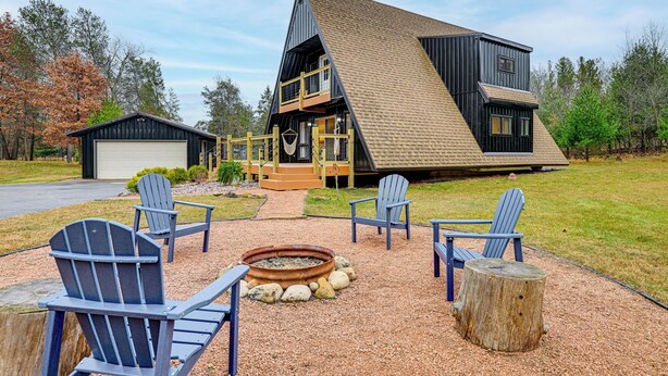 Una casa moderna de dos pisos con un amplio balcón, zona de estar exterior con sillas Adirondack y una chimenea.