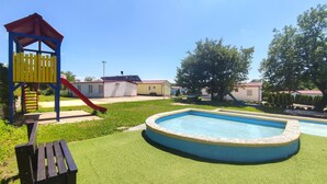 Una piscina rodeada de césped artificial, un tobogán y un pequeño banco de madera.
