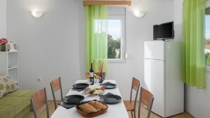 A dining area with a table set for four, a refrigerator, a television on top, and a window with green curtains. - Amazing home in Tinjan (Tinjan)