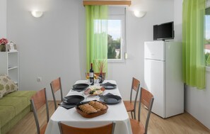 A dining area with a table set for four, a refrigerator, a television on top, and a window with green curtains. - Awesome home in Tinjan (Tinjan)