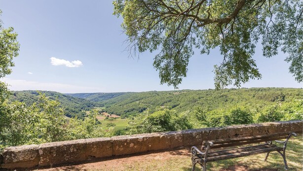 Um banco com vista para uma paisagem montanhosa, coberta por vegetação densa e com céu limpo.