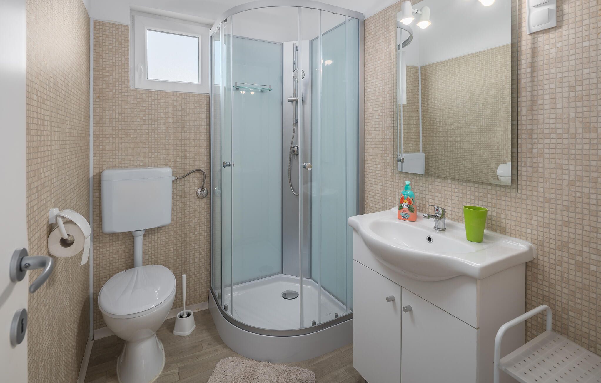 A modern bathroom with a glass-enclosed shower, a toilet, and a sink with a mirror above.