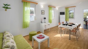Ein modernes Wohnzimmer mit einem grünen Sofa, einem Esstisch für zwei Personen und einem kleinen weißen Tisch mit zwei Tassen.