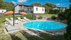 Ein Swimmingpool mit Liegestühlen und Sonnenschirmen, umgeben von einem Garten und einem Haus mit rotem Dach.
