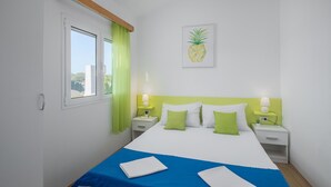 Habitación de hotel con cama, cortinas verdes, una obra de arte con piña y dos lámparas de noche.