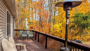 A wooden deck with Adirondack chairs, a patio umbrella, and a portable heater. - 3 Bedroom house w/ lake access, hot tub and pet friendly! (Grawn)