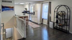 A modern kitchen with white cabinets, a dining area with a wooden table, and a staircase leading to an upper floor. - 3 Bedroom house w/ lake access, hot tub and pet friendly! (Grawn)