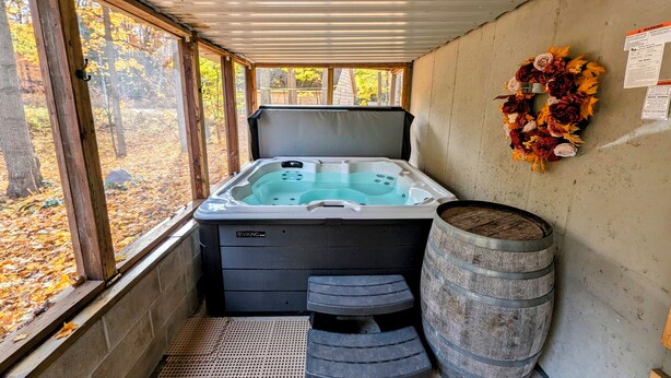 A hot tub with a wooden bench and a barrel, a wreath on the wall, and a view of autumn leaves through the windows. - 3 Bedroom house w/ lake access, hot tub and pet friendly! (Grawn)
