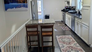 A modern kitchen with a central island, white cabinetry, and a patterned rug. - 3 Bedroom house w/ lake access, hot tub and pet friendly! (Grawn)