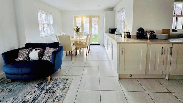 Un salón amplio con un sofá azul, una zona de comedor con una mesa y sillas, y una cocina con armarios y una encimera.