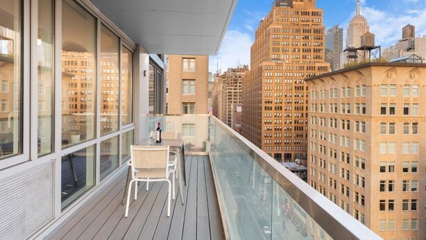 A balcony with a table and chairs, overlooking a cityscape with tall buildings.