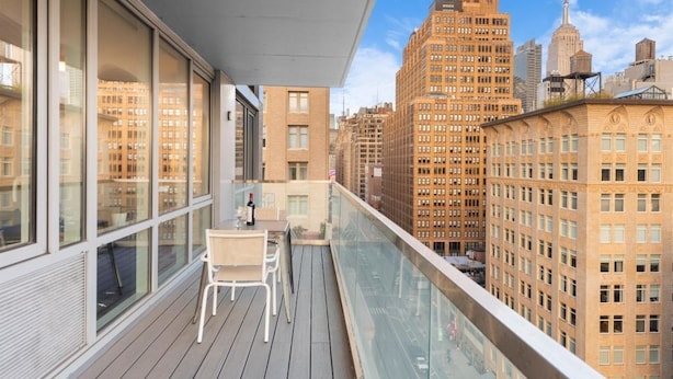 A balcony with a table and chairs, overlooking a cityscape with tall buildings. - Elegant 2BR SilverDoor Chelsea Condo (New York)