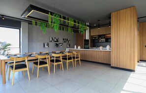 A modern dining area with wooden chairs and tables, a kitchen area with wooden cabinets, and hanging plants. - w* | Ravishing 2BR w/ Balcony  in Miraflores (Miraflores)
