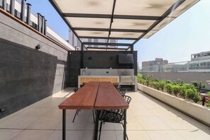 A rooftop terrace with a wooden table and chairs, a grill, and a view of the city. - w* | Ravishing 2BR w/ Balcony  in Miraflores (Miraflores)