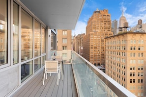A balcony with a table and chairs, overlooking a cityscape with tall buildings.