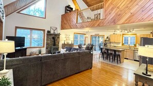 A spacious living area with a large sofa, a fireplace, and a dining area with bar stools. - Winnipesaukee Retreat | Hot Tub | Suissevale Beach (Moultonborough)