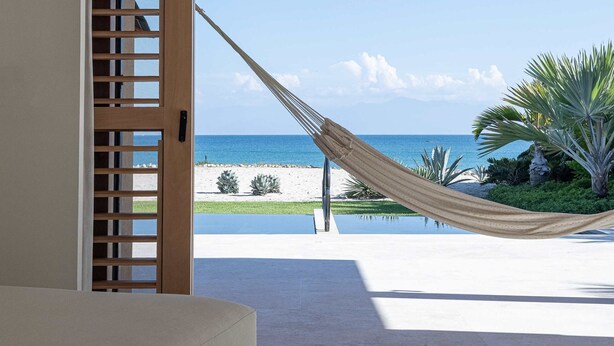 Una habitación con un ventanal grande, una hamaca y vista a la playa.