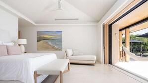 Un dormitorio moderno con una cama grande, un sofá, un cuadro de playa y vistas al exterior.