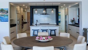 Una cocina moderna con una isla central, un comedor con mesa redonda y sillas, y una araña.