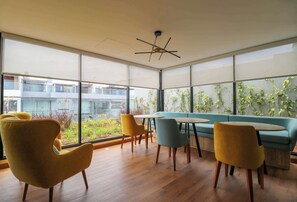 A modern interior with large windows, wooden flooring, and a mix of yellow and blue chairs around a central table. - w* | Dreamlike 2BR w/ Balcony in Miraflores (Miraflores)
