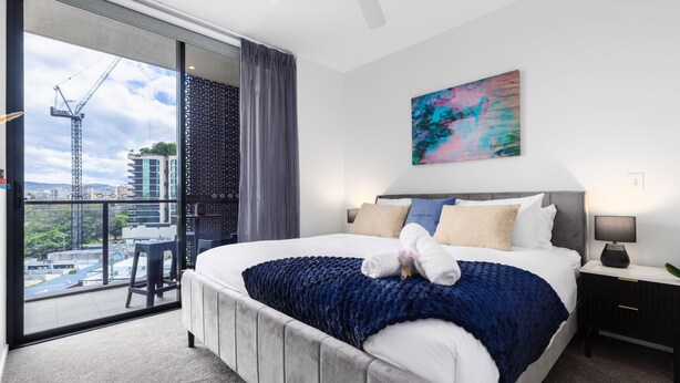 Ein modernes Hotelzimmer mit einem großen Bett, einem Balkon mit Blick auf die Stadt und einem farbenfrohen abstrakten Gemälde an der Wand.
