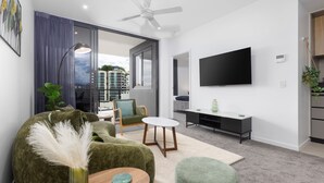 Ein modernes Wohnzimmer mit Flachbildfernseher, grünen Möbeln und Blick auf die Stadt.