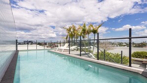 Ein Pool auf dem Dach mit klarem, blauem Wasser, umgeben von Liegestühlen und Palmen, unter einem teils bewölkten Himmel.
