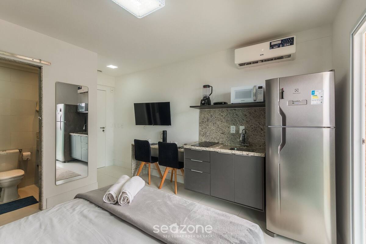 A compact hotel room with a bed, a small kitchenette, a flat-screen TV, and a bathroom.