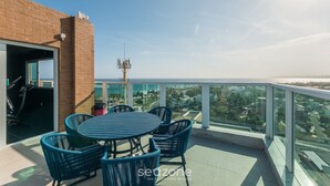 Un balcon doté d’une balustrade en verre, une table avec des chaises et une vue sur la ville et l’océan.